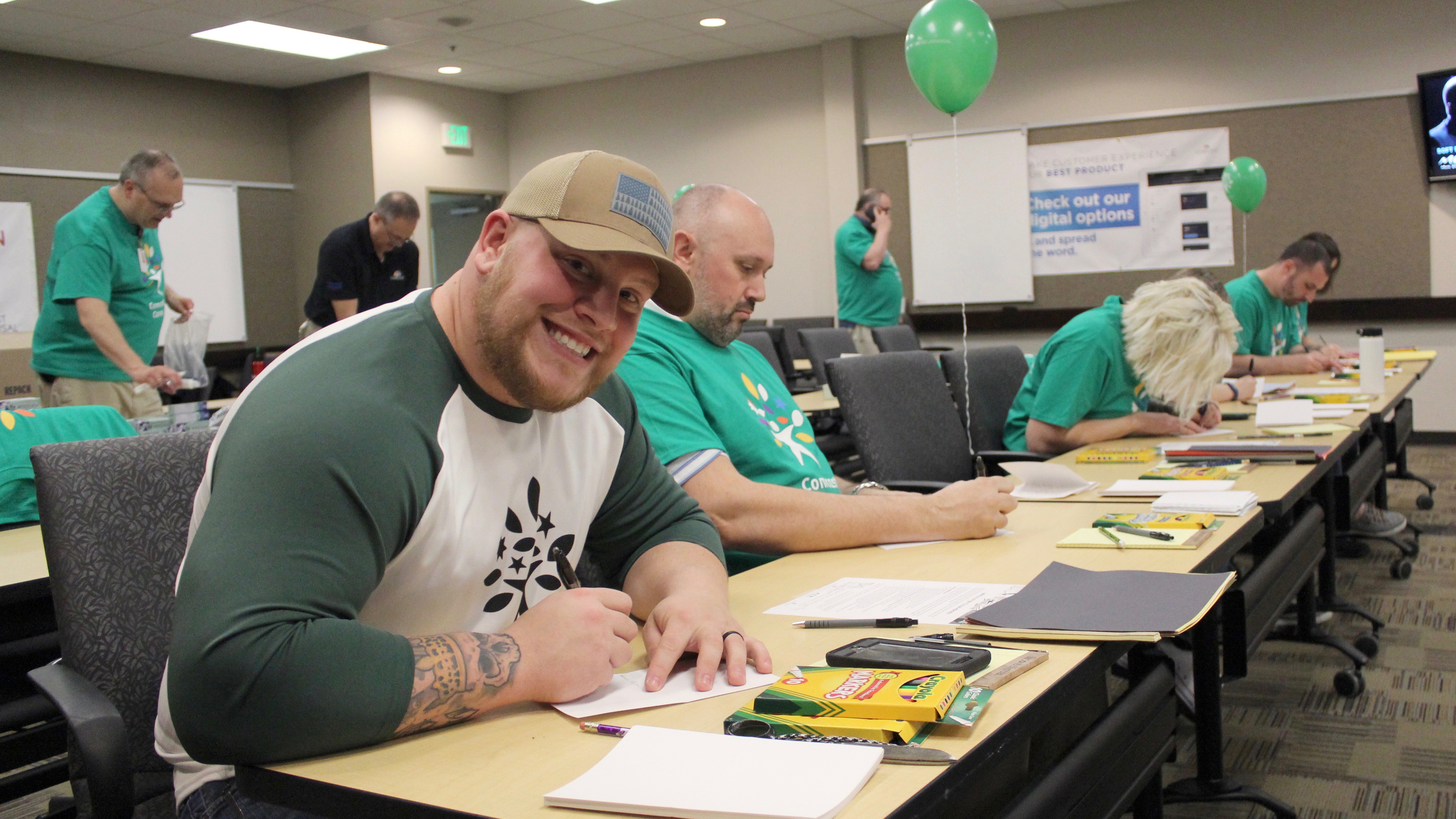 Cody King and other Comcast Cares Day volunteers sit at desks and write on piece of paper.