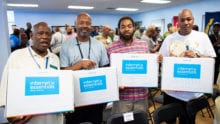 Four veterans hold up their Internet Essentials laptops at an event in Detroit.