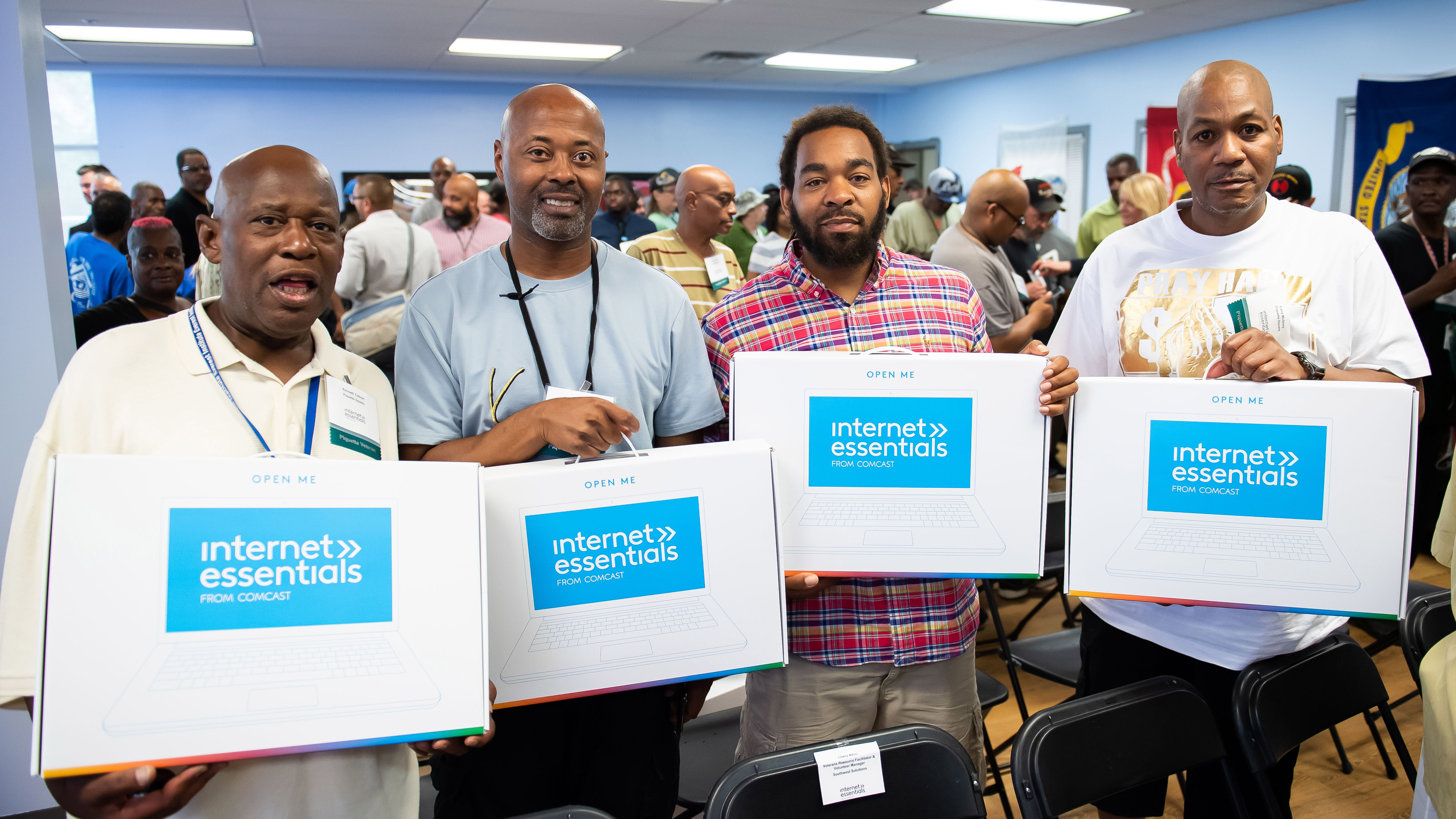 Four veterans hold up their Internet Essentials laptops at an event in Detroit.