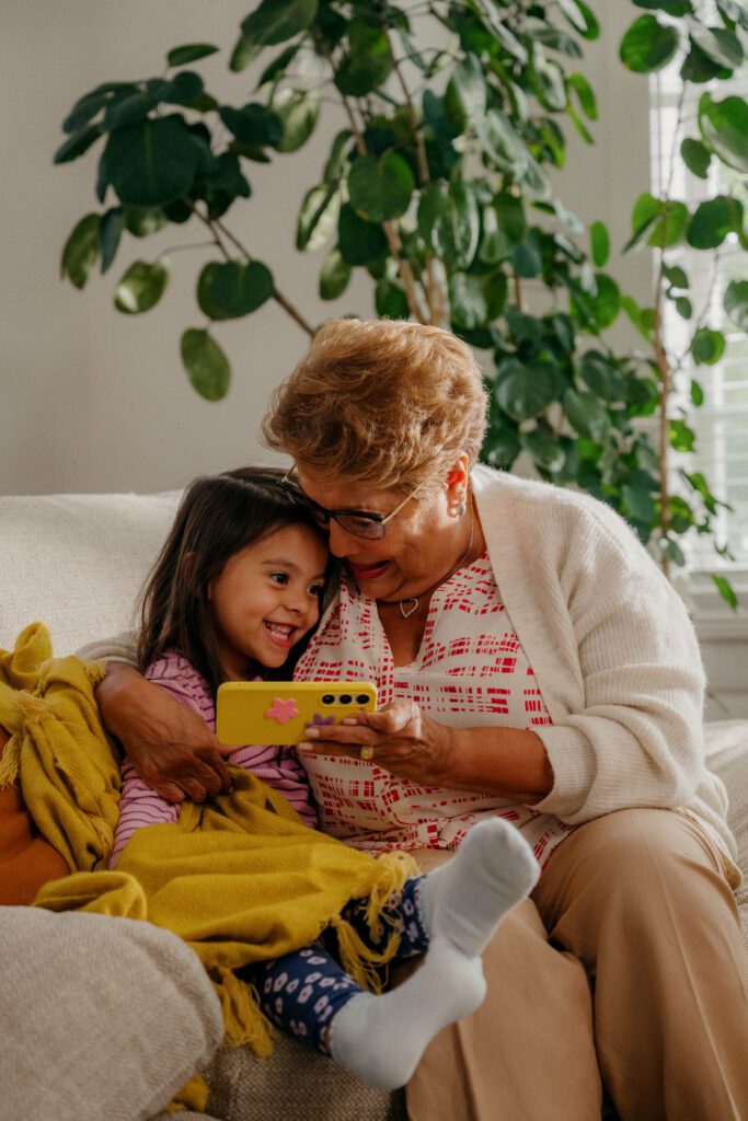 Child and woman sit on a couch, looking at a cell phone together
