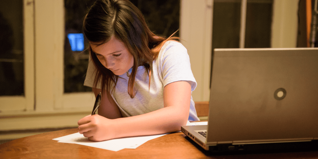 A young student writes on a piece of paper next to her laptop. Xfinity's Internet Essentials offers a low-cost internet and mobile plan.