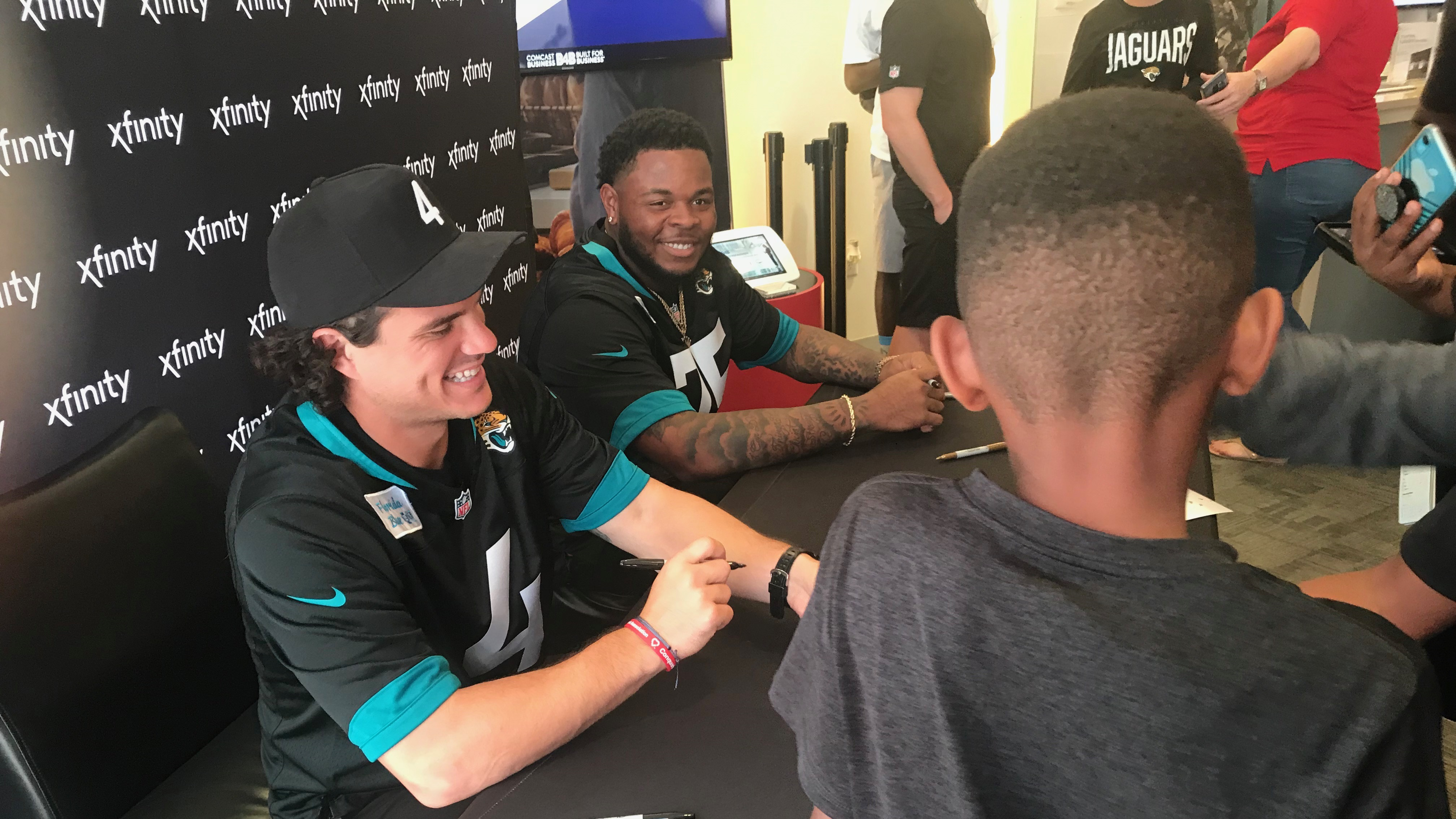 Members of the Jacksonville Jaguars sign autographs at an Xfinity event.