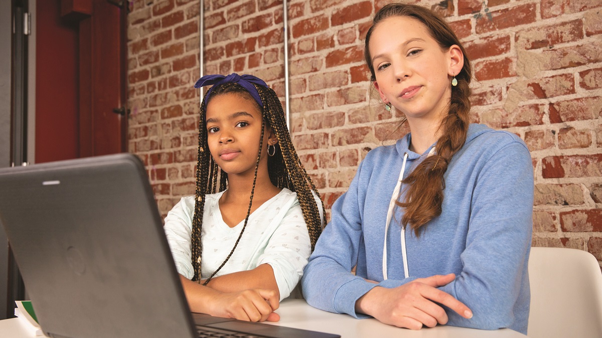 two teen girls at a table, looking at a laptop
