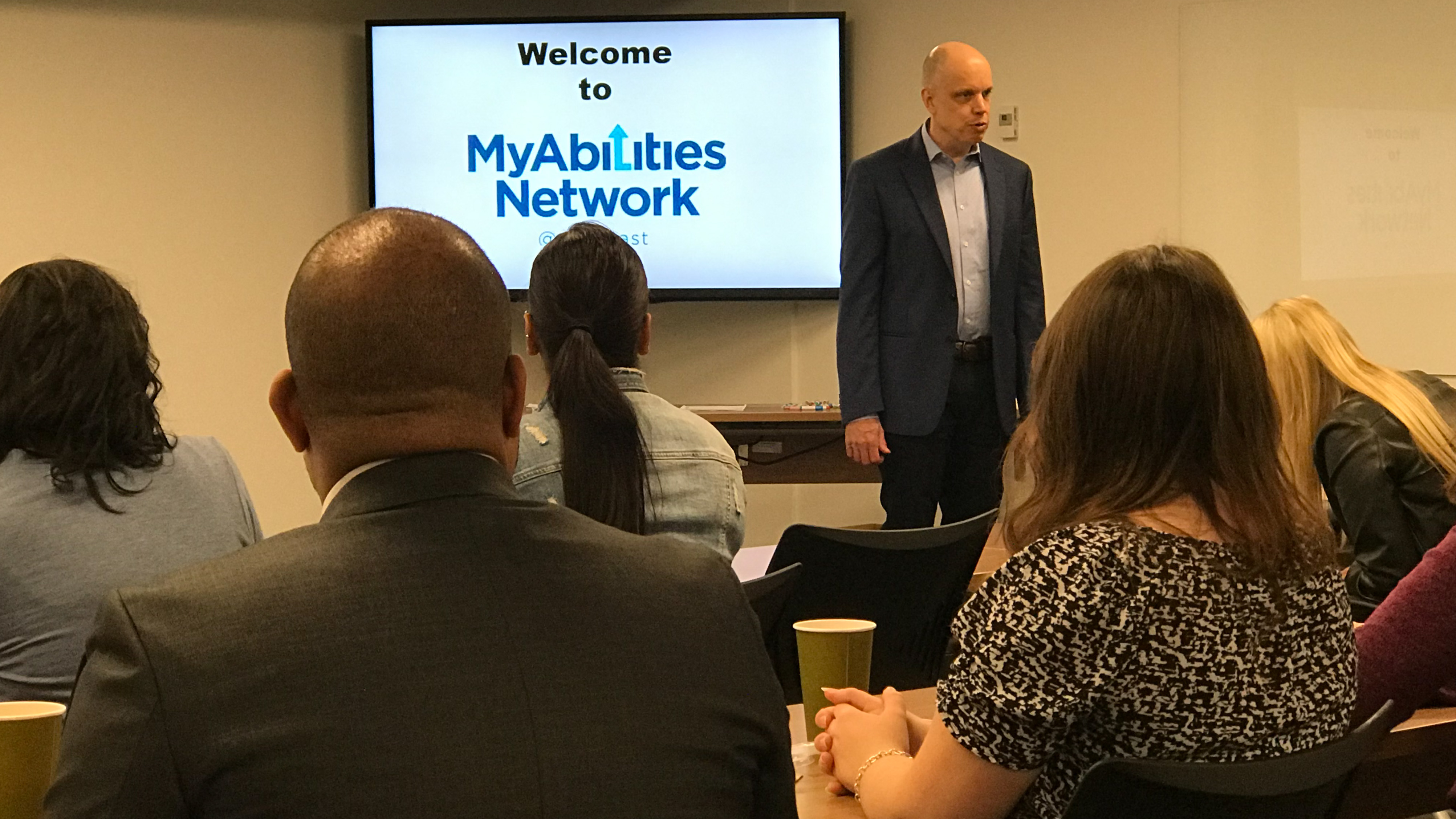 Tom Wlodkowski speaking to a group of employees with a screen behind him displaying the MyAbilities Network logo