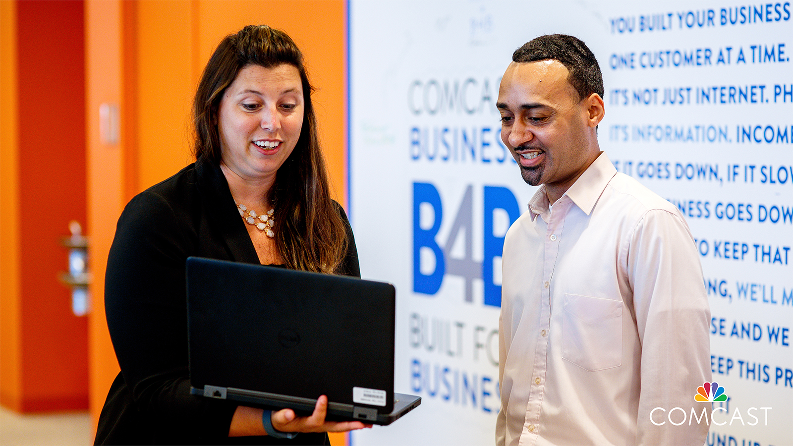 Woman showing a man something on her laptop as they stand in front of Comcast Business logo