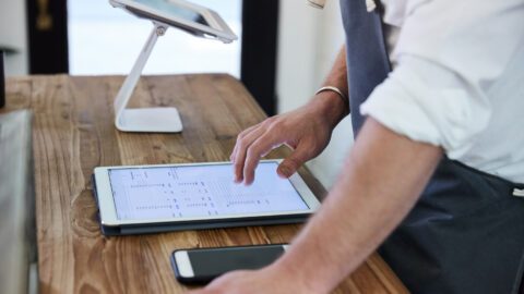 Person typing onto digital tablet with mobile phone sitting in front of them