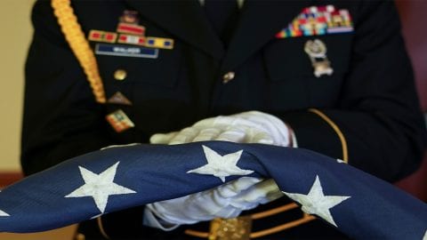 A member of the armed forces holds an American flag.