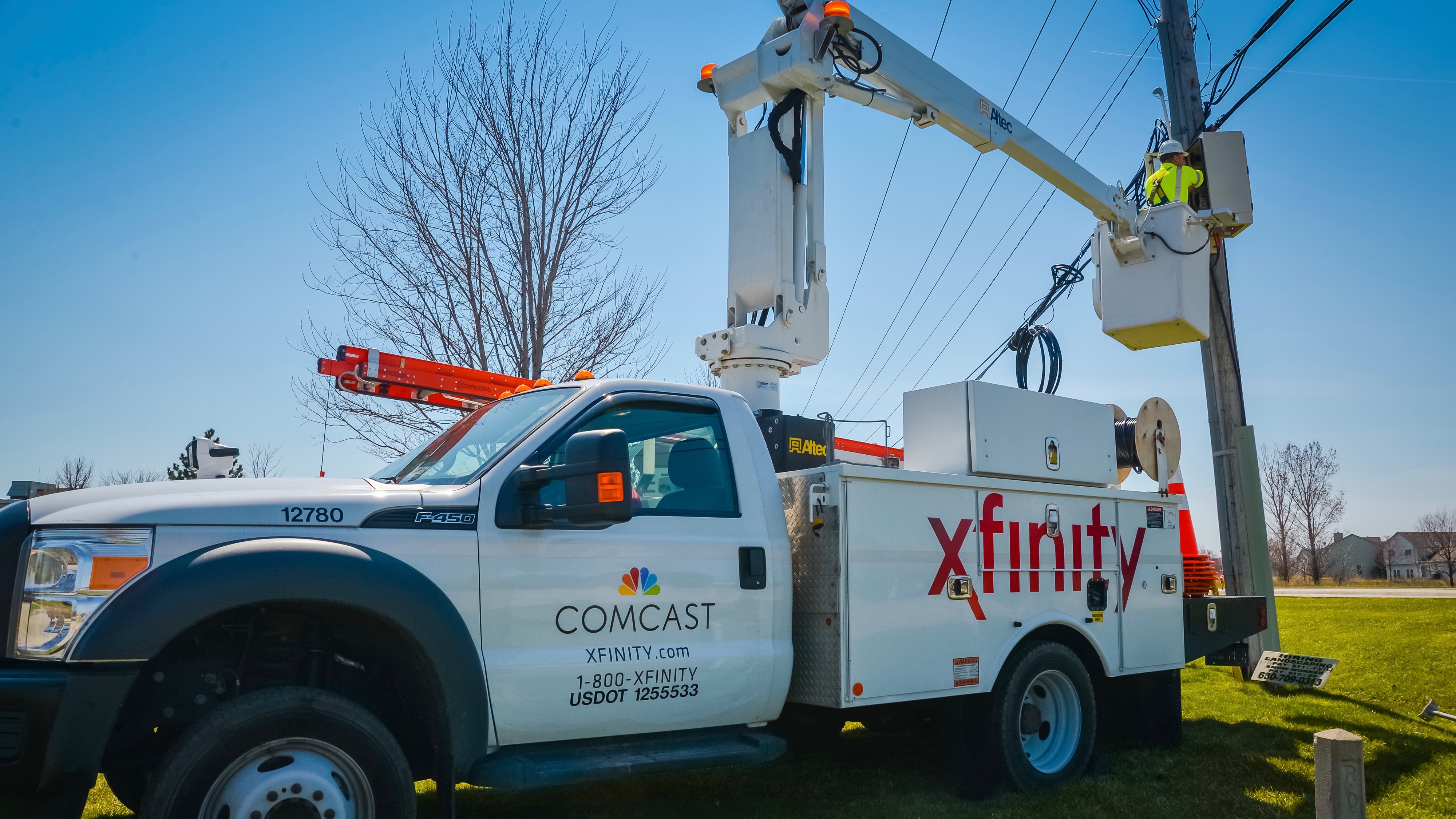 An Xfinity truck extends its crane to reach machinery on a telephone pole.
