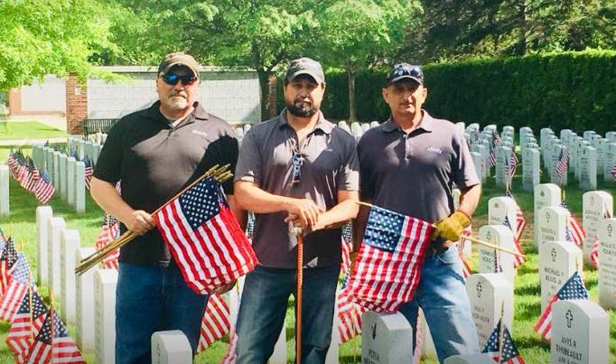 Three Xfinity employees hold American flags as they stand in a graveyard.