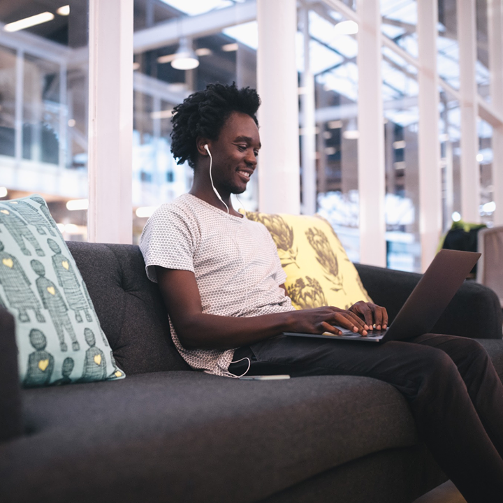 A person sits on a couch as they use a laptop.