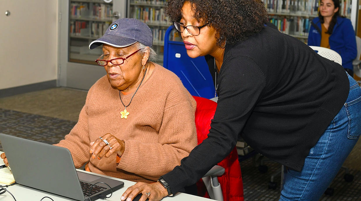 Volunteer assisting an older woman with her laptop.