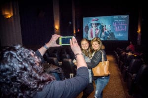 person taking photo of two people standing in front of movie screen