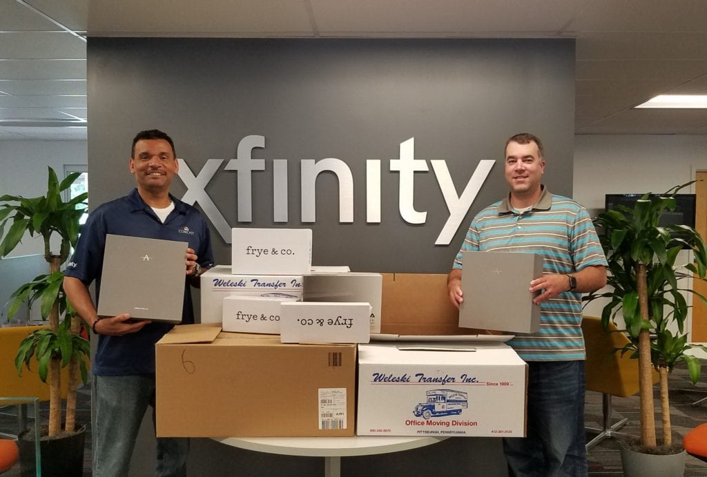 Two Comcast employees holding boxes of donated shoes