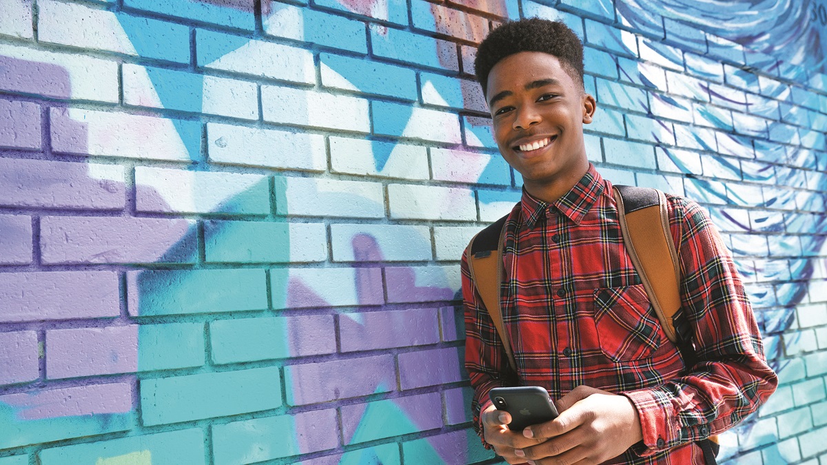 teen boy holding smartphone, leaning against colorfully painted wall