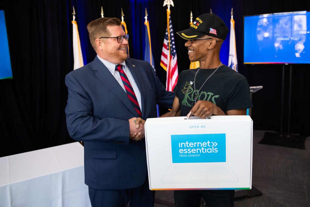 smiling man shaking the hand of a military veteran while handing him a laptop