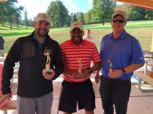 three men holding trophies at a golf course