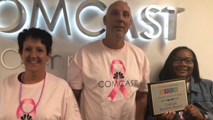 employees holding a plaque in front of Comcast logo
