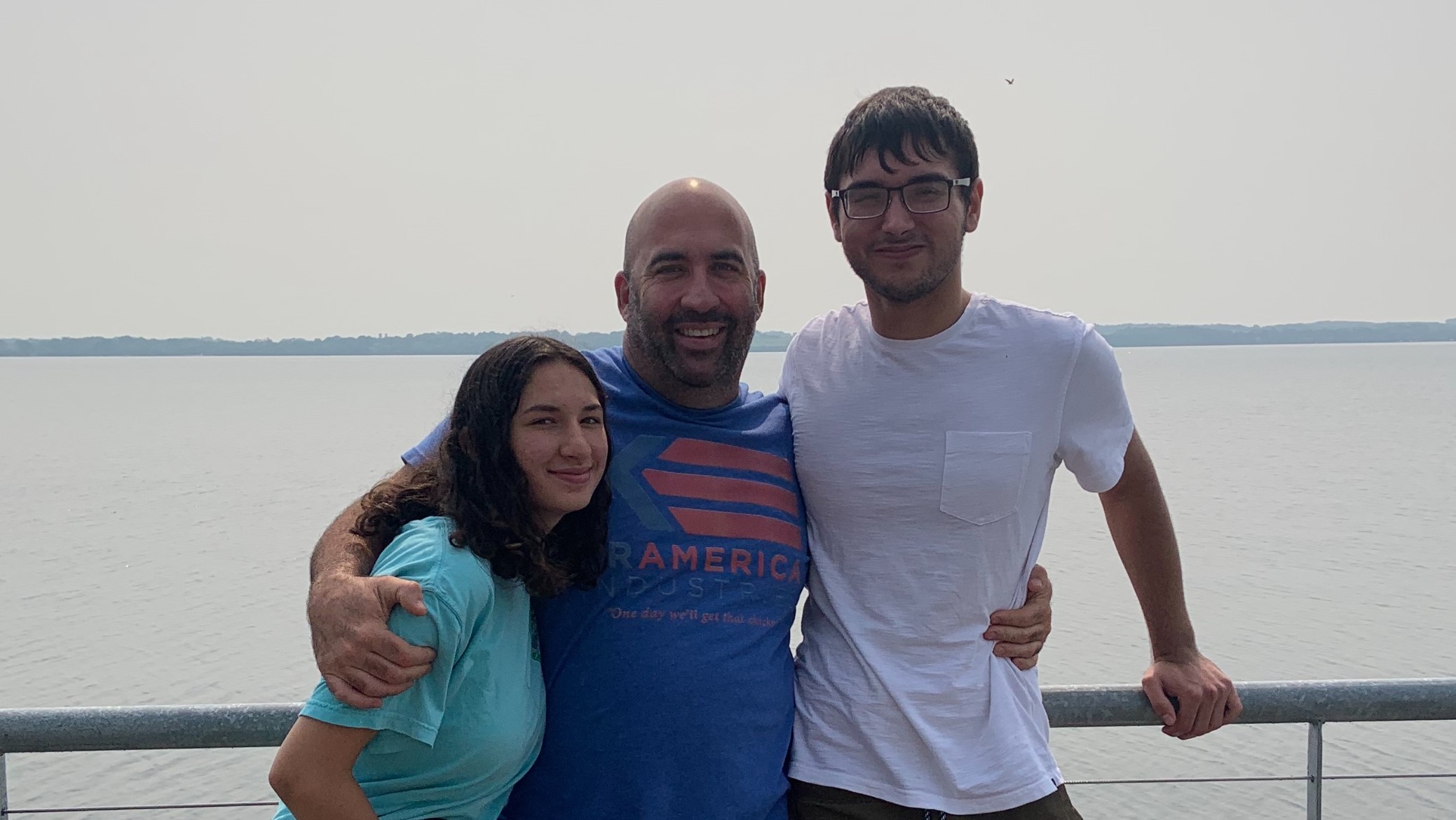 Man and two teens standing in front of a lake